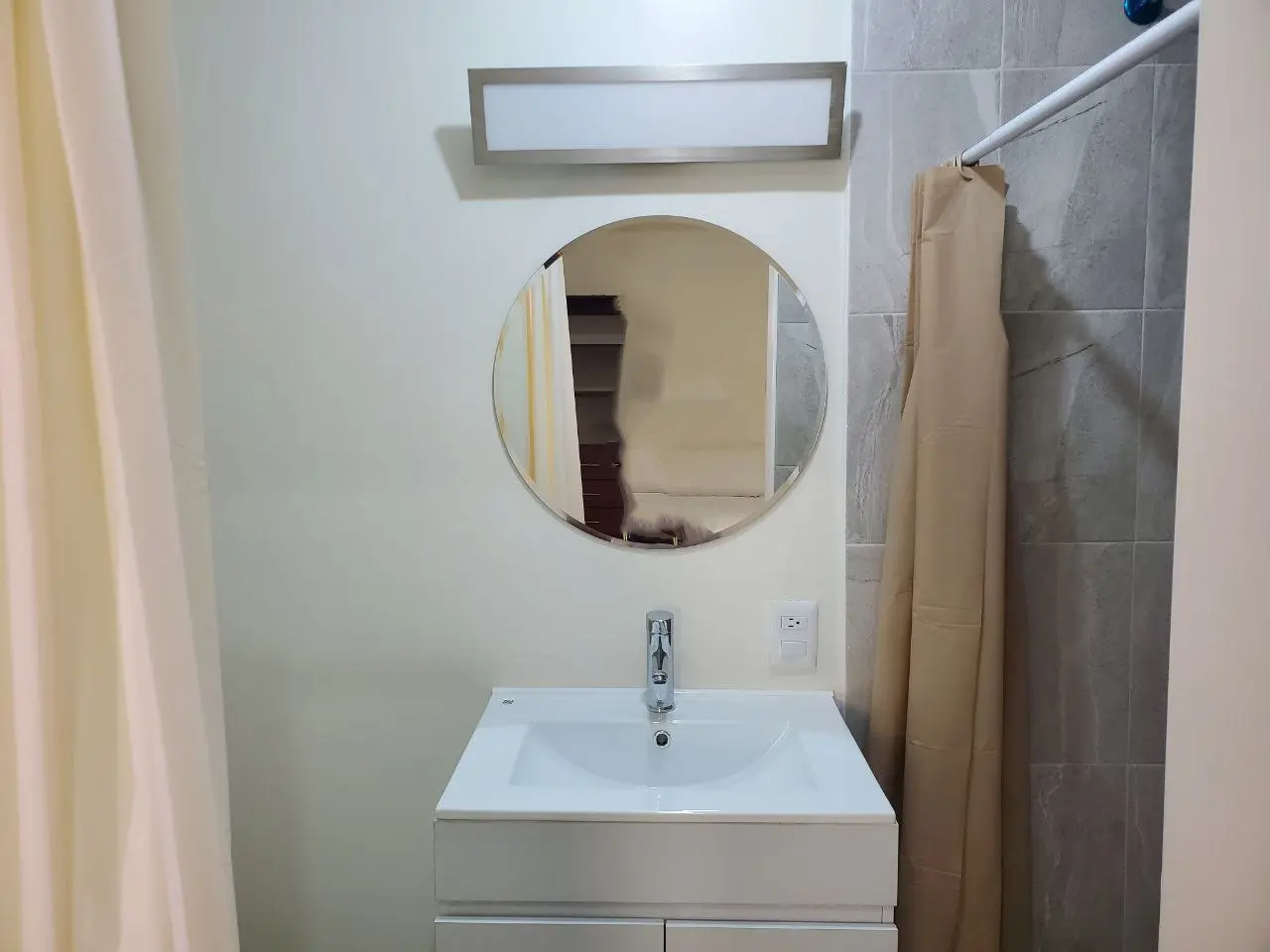 Baño privado con lavabo, espejo redondo y regadera en la habitación con cama matrimonial